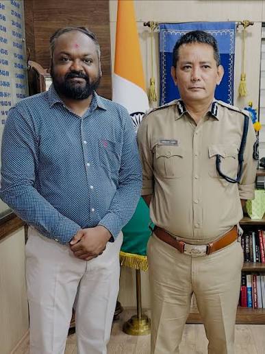 Wabang Jamir, IPS, in uniform receiving a visitor at his office beside the national flag.